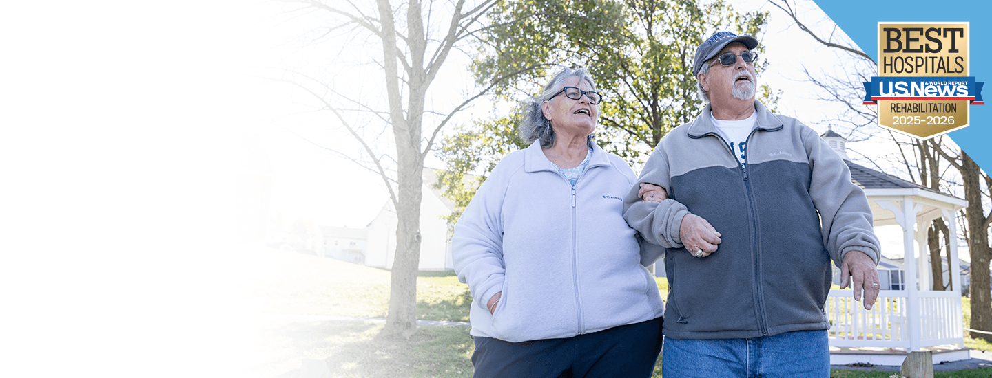 Senior-age man and woman walking outside arm in arm.